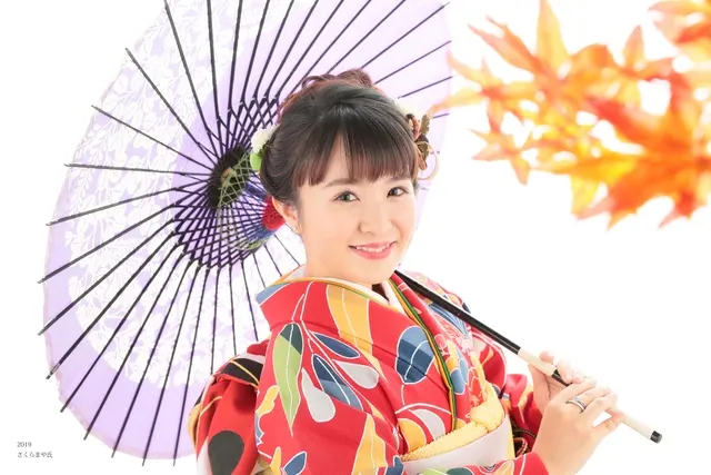 紫の和傘と紅葉を背に微笑む着物姿の女性