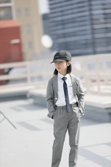 屋上でキャップとスーツをまとい遠くを見る男の子