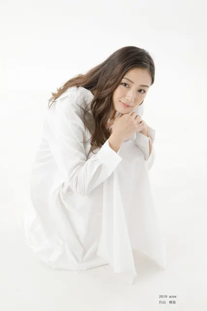 白いシャツドレスで膝を抱え柔らかく微笑む女性