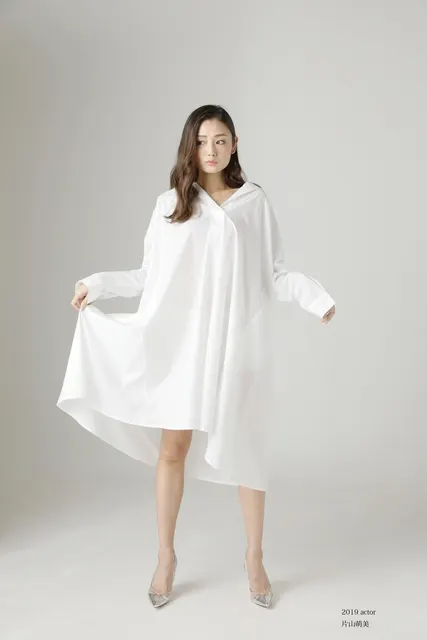 白いシャツワンピースの裾を広げて立つ女性