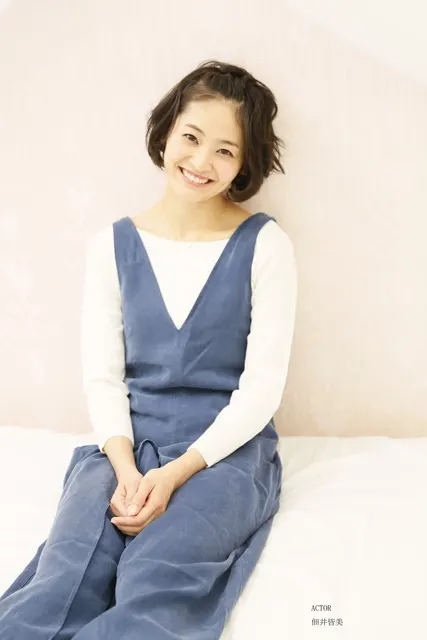 ベッドに座り微笑む女性、ネイビーのワンピース姿