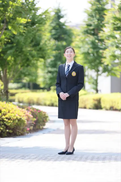 緑の並木を背に微笑むスーツ姿の女性、別ポーズ