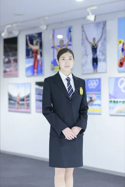オリンピック写真が並ぶギャラリーに立つスーツ姿の女性