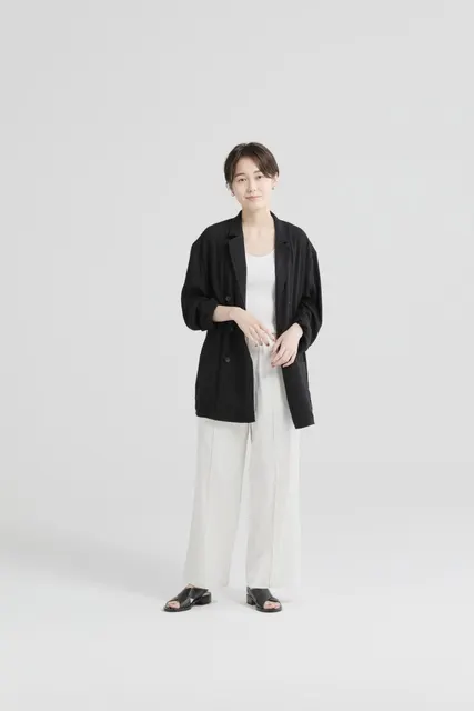 黒いテーラードジャケットに白パンツで凛と立つ女性