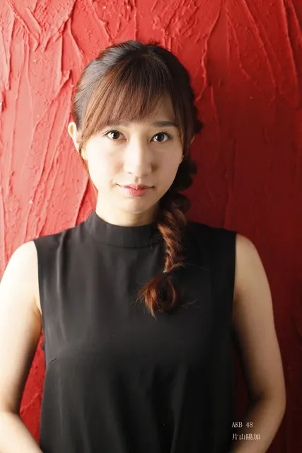 赤い壁を背に編み込み髪の女性が微笑むアップ