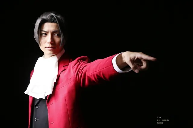 赤い衣装で舞台さながらに指を差す男性